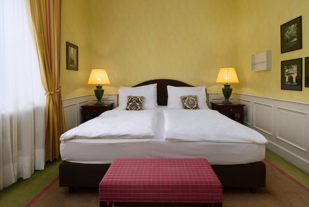 Ložnice s dvoulůžkem, zelenými lampami a bordově červenou lavicí